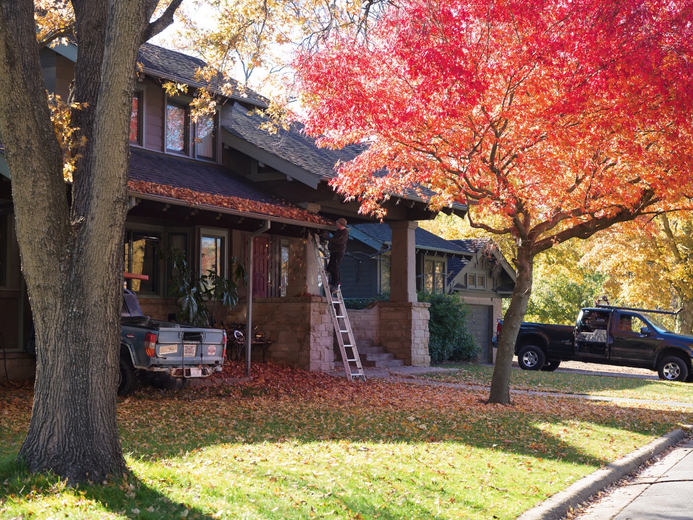 A worker on a ladder cleaning fall leaves out of a home's gutters